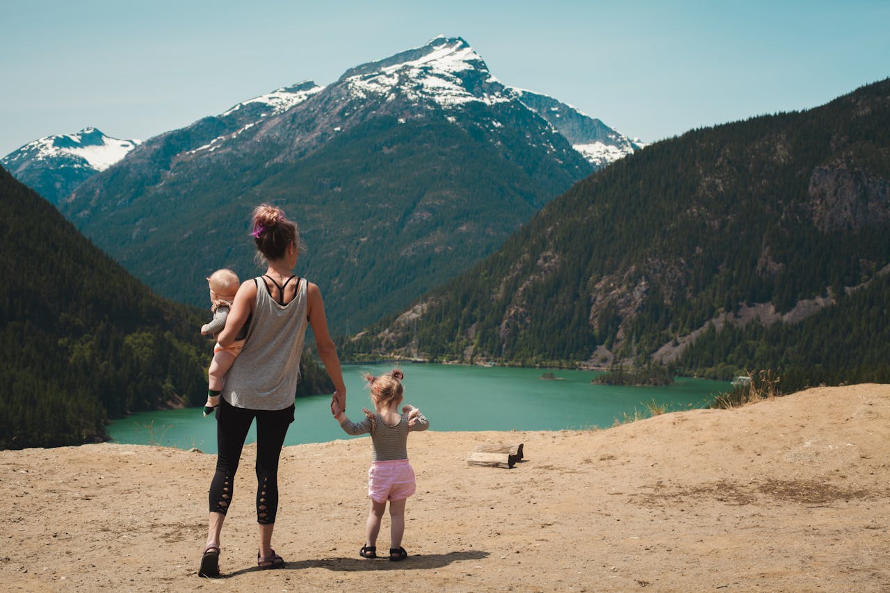 gallery-2 A mother with two children enjoys a scenic mountain and lake view during a sunny outdoor hike.