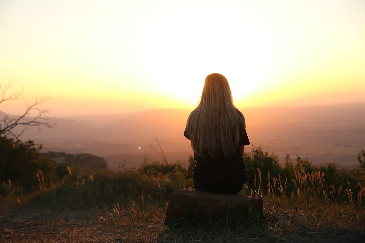 our-services-2 Woman sitting in nature, watching sunset over fields. Peaceful and serene outdoor scene.